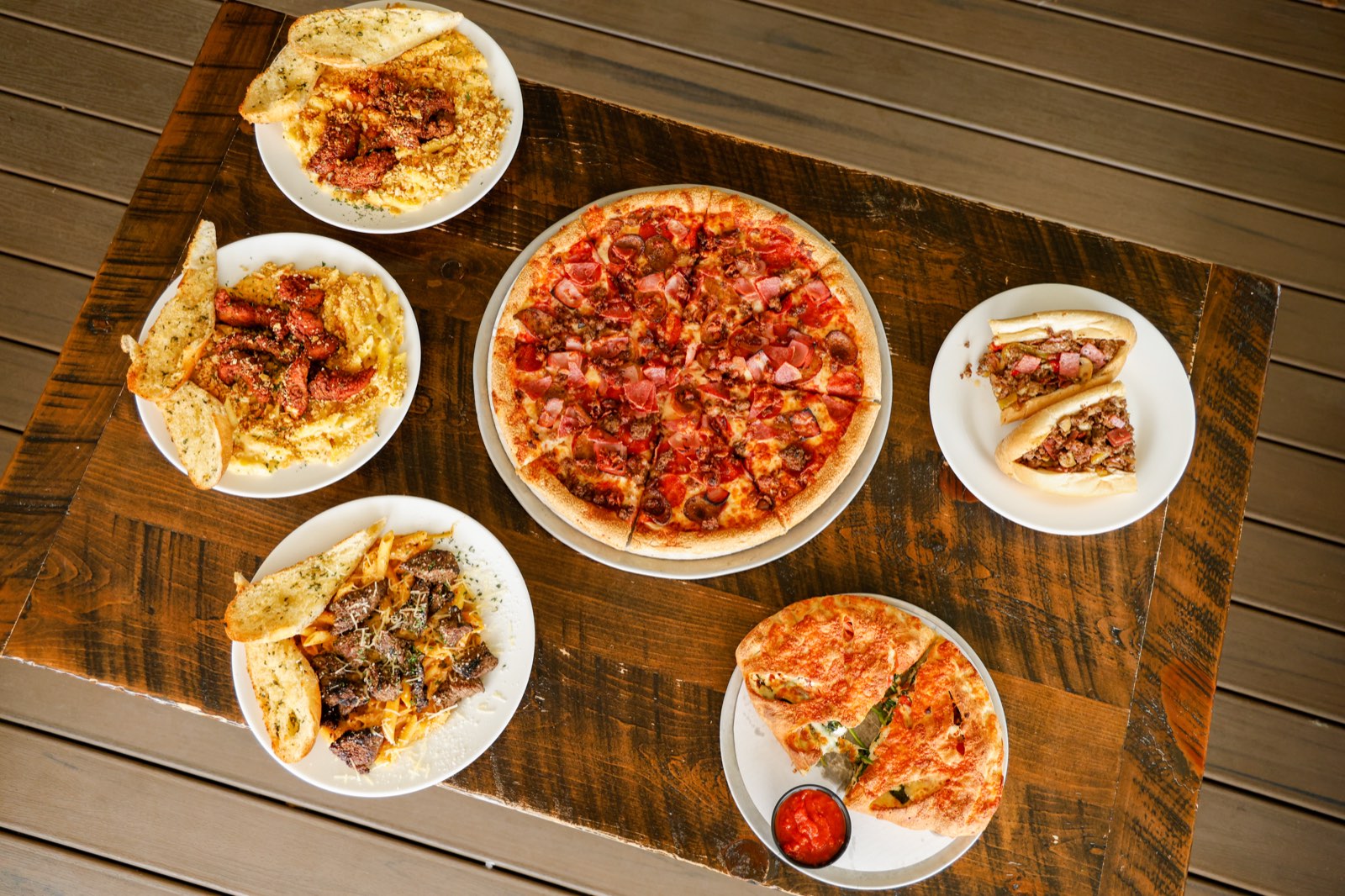 Overhead spread of pizza, pasta, a calzone and a steak sub