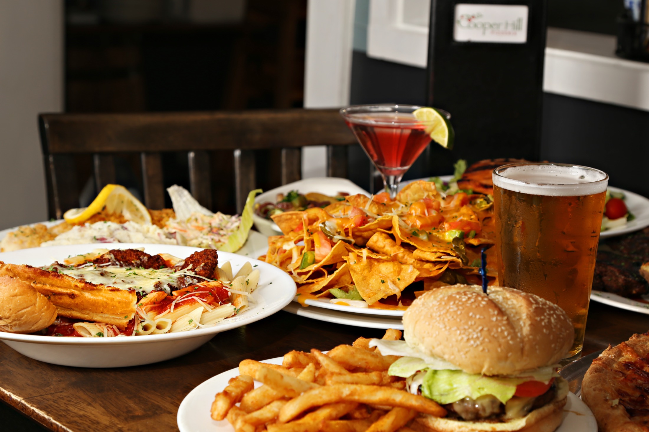 A table full of Cooper Hill favorites: chicken parm, nachos, a burger with fries, a cosmo and a cold draft beer
